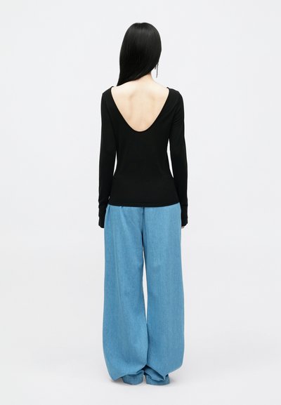 Top preto de mangas compridas com um profundo decote nas costas, combinado com calças de ganga em azul claro e folgadas, apresentando um corte descontraído e pernas largas.