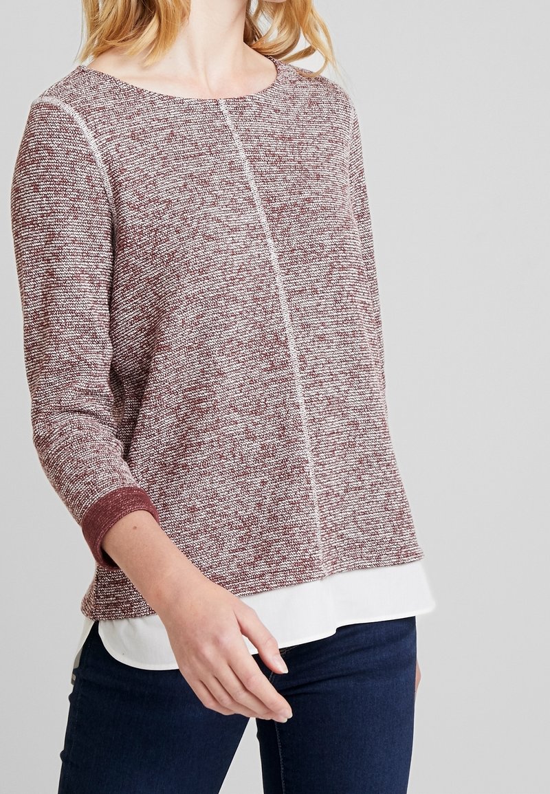 Top de punto en burdeos y crema con un patrón texturizado, cuello redondo, mangas tres cuartos y un dobladillo blanco de capas.