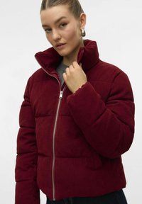 Burgunderfarvet fløjl puffersjakke med høj krave, lynlås lukning og syede paneler. Har en blød tekstur og en let cropped design.