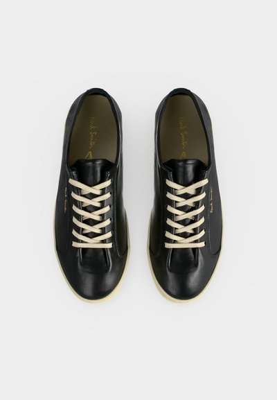 Paire de baskets en cuir noir avec des lacets blancs et des semelles beiges vues de dessus sur un fond uni.