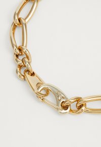 Gold-toned metal chain necklace featuring links of varying shapes, a secure clasp with a logo detail, and a smooth, polished finish.