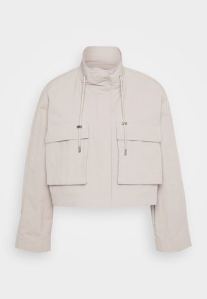 Cropped jacket in light beige fabric with a high collar, two front flap pockets, and adjustable drawstrings for a secure fit.