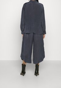 Dark gray crinkled fabric outfit featuring a long-sleeve top and wide-leg trousers, paired with black ankle boots with a pointed toe.