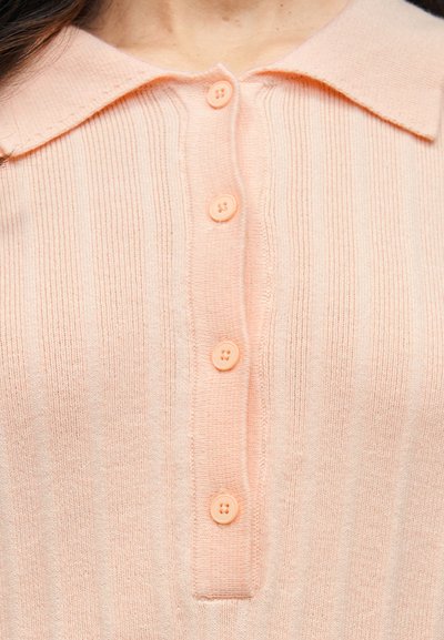 Ανοιχτό ροζ πλεκτό πόλο πουλόβερ με ραβδώσεις, που διαθέτει γιακά και έξι κουμπιά στο εμπρόσθιο τμήμα. Μαλακή υφή και εφαρμοστή γραμμή.