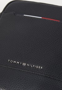 Schwarzer strukturierten Leder-Dokumentenhalter mit einem metallic "TOMMY HILFIGER" Logo und einem roten, weißen und blauen Kartensteckplatz-Detail.