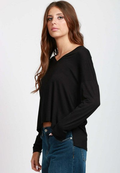 Top nero a maniche lunghe con scollatura a V. Realizzato in materiale morbido, presenta una vestibilità rilassata e una lunghezza corta, abbinato a jeans a vita alta.