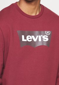 Sudadera burdeos con un gran logo gris de Levi's. Fabricada en un tejido suave, con cuello redondo y mangas largas.