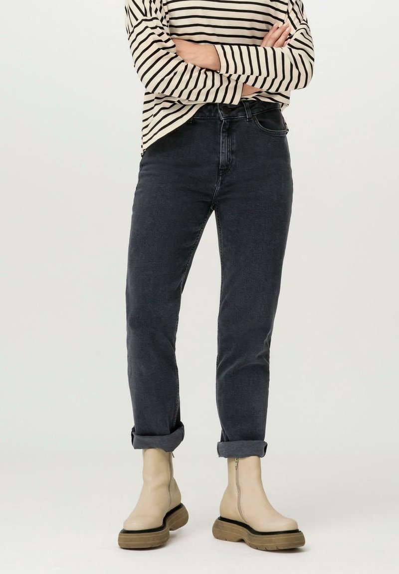 Jeans en denim délavé foncé à coupe slim avec des revers roulés, associés à des bottines beiges avec une semelle plateforme noire et un détail de fermeture éclair.