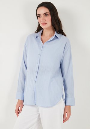 Light blue button-up shirt with a textured fabric, long sleeves, and a classic collar. Features a straight cut and side slits for ease.