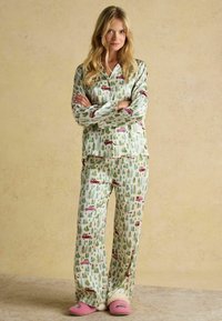 Pajama set in light green fabric featuring a forest and car print, long sleeves, and comfortable fit, paired with pink slippers.