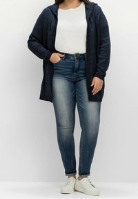 Granatowy sweter z dzianiny z kapturem, jasnoszara koszulka i średnio niebieskie dżinsy o wysokim stanie, w połączeniu z białymi sneakersami.