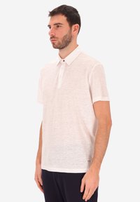 Polo shirt corto a maniche corte color beige chiaro con tessuto testurizzato, patta con tre bottoni e colletto classico. Sottile etichetta del marchio all'orlo.