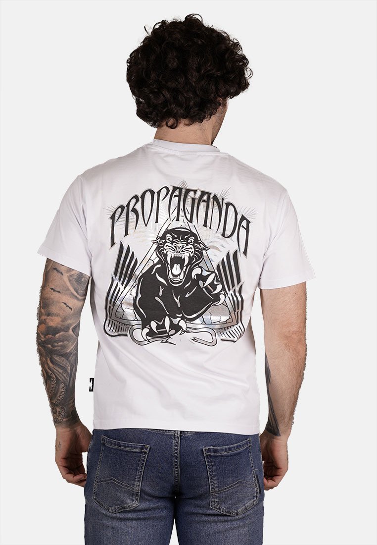 T-shirt bianca in cotone con una grafica nera di un pantera ruggente e il testo "PROPAGANDA" in carattere grassetto sul retro. Maniche corte, vestibilità casual.