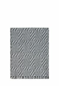 Coperta tessuta in bianco e nero con un motivo geometrico a zigzag, rifinita con bordi frangiati e una consistenza morbida.