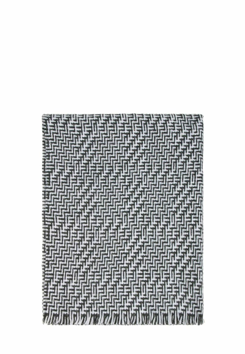 Coperta tessuta in bianco e nero con un motivo geometrico a zigzag, rifinita con bordi frangiati e una consistenza morbida.