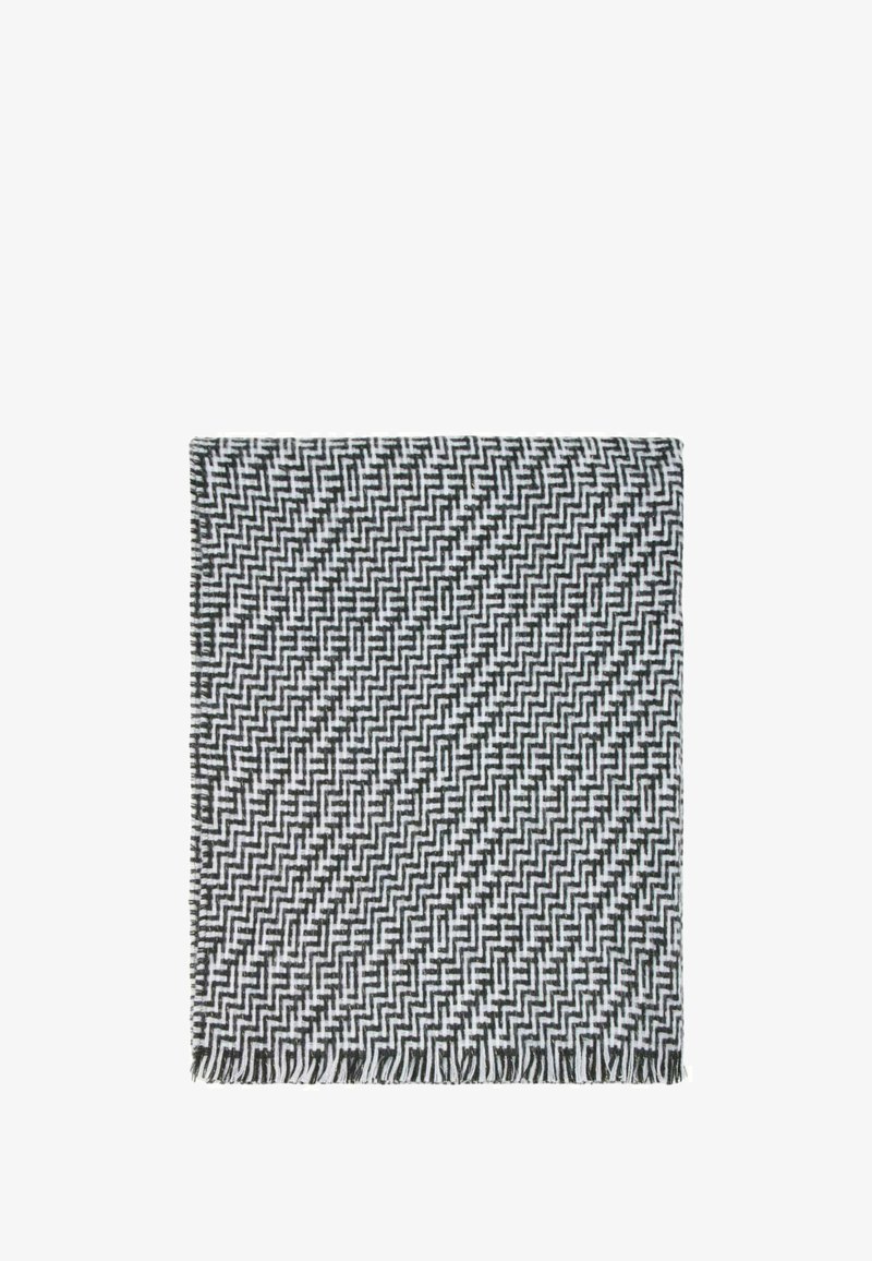 Coperta tessuta in bianco e nero con un motivo geometrico a zigzag, rifinita con bordi frangiati e una consistenza morbida.
