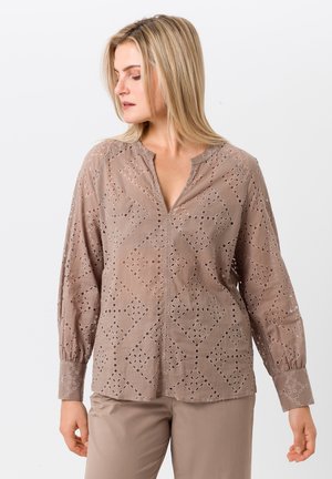 Blouse beige clair avec des motifs en losanges découpés, manches longues et coupe décontractée. Tissu légèrement texturé et patte de boutonnage partielle.