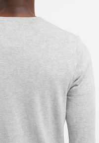 Suéter gris de manga larga con una textura suave, escote redondeado y detalles de costura sutiles en los puños y el dobladillo.