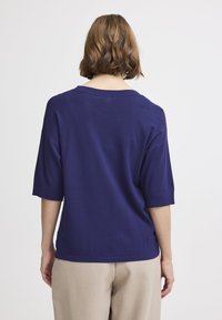 Marineblauwe gebreide trui met korte mouwen, relaxte pasvorm, brede halslijn en een gladde textuur, gecombineerd met lichtgrijze broeken.