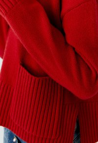 Rode gebreide trui met ribbeltextuur, voorzien van een grote voork pocket en losse mouwen. Zacht, dik materiaal biedt warmte.
