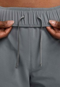 Grijze elastische tailleband met trekkoord, gladde stof, twee handposities, eenvoudig ontwerp. Geen zichtbare patronen of hardware-details.