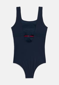 Μπλε ναυτικό ολόσωμο μαγιό με φαρδιές τιράντες, άνοιγμα στην πλάτη και κόκκινες διακοσμητικές λεπτομέρειες στη εσωτερική ταινία. Ομαλό, ελαστικό ύφασμα.