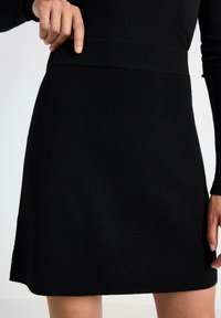 Vestito nero a maglia con cintura a coste, di lunghezza corta e texture morbida; il tessuto sembra leggero e leggermente elastico.