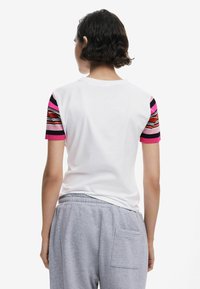 White cotton t-shirt with colorful striped knit sleeves in pink, red, and black. Casual fit, features round neckline, back view.