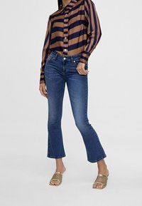 Uppvikta jeans i medelblå denim, med mid-rise och klassisk femficksdesign. Kombinerade med en randig, knäppt blus.