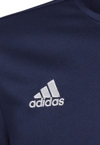 Tissu bleu marine avec une texture lisse présentant un logo Adidas brodé en blanc sous la forme de trois bandes et le nom de la marque.