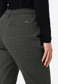 Gray plaid trousers made from textured fabric, featuring a back pocket and a metal logo accent on the waistband.