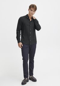 Mørk grå skjorte med knapp foran, laget av teksturert stoff, slim fit, brystlomme, kombinert med marineblå bukser og mørke sko, stående på en hvit bakgrunn.