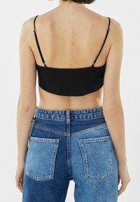 Zwarte cropped tanktop met dunne verstelbare bandjes, gecombineerd met highwaisted blauwe denim jeans met contrasterende kleuren van de zakken en naden.
