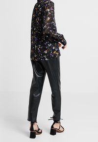 Blusa nera trasparente con stampa floreale multicolore, abbinata a pantaloni aderenti neri in ecopelle e sandali neri con tacco e lacci alla caviglia.