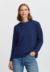 Maglione a maniche lunghe blu navy realizzato in tessuto testurizzato con scollatura rotonda e vestibilità comoda, abbinato a jeans in denim azzurro chiaro.