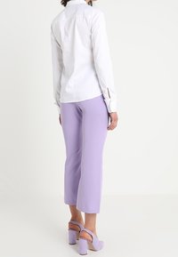 White button-up shirt; light purple cropped pants; chunky lavender heels; smooth fabric; tailored design; visible button details; relaxed fit.