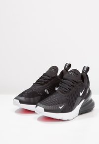 Scarpe da ginnastica sportive nere con superiore in rete, punta arrotondata e suola bianca. Presentano dettagli con logo e un tallone imbottito per supporto.