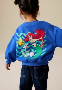 Sweat-shirt bleu avec un grand motif représentant une sirène aux cheveux roux et un poisson jaune, agrémenté d'accents floraux et de coquillages, avec poignets et ourlet côtelés.