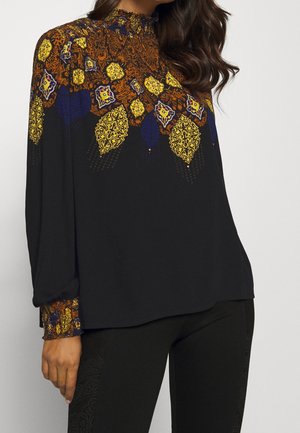 Zwarte blouse met een hoge halslijn, lange mouwen en een kleurrijk patroonaccent in oranje, geel en blauw rond de schouders en manchetten.