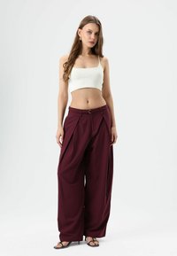 Maroon wide-leg trousers with pleats, featuring a belted waist. Paired with a fitted white crop top and black sandals. Smooth texture.