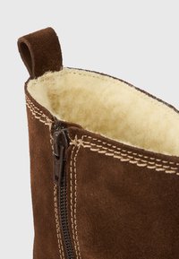 Καφέ μπότες από σουέτ με απαλή κρεμ εσωτερική επένδυση, διαθέτουν κλείσιμο με φερμουάρ και αντίθετη ραφή σε ταν απόχρωση κατά μήκος της επάνω άκρης.