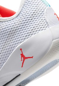 Gros plan d'une chaussure de sport blanche avec logo Jumpman rouge, dessus en mesh texturé, et semelle translucide.