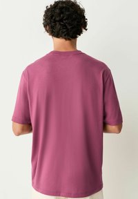 Kortærmet t-shirt i afdæmpet mauve bomuld. Har en klassisk rund hals med en glat tekstur og en afslappet pasform. Ingen synlige logoer eller mønstre.
