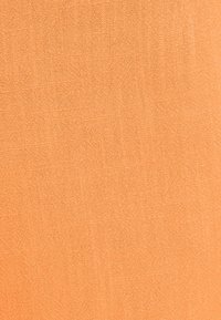 Světlé oranžové látce se hladkým povrchem, s jemným tkaným vzorem. Materiál vypadá lehký a prodyšný.