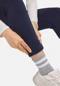 Leggings azul marino con una textura suave, con dobladillo acampanado, combinados con calcetines a rayas grises y blancas y zapatillas blancas.