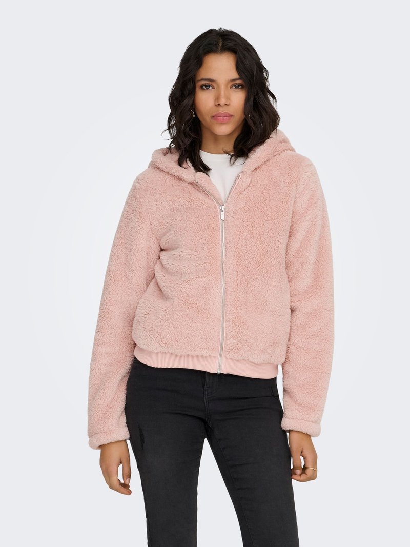 Vaaleanpunainen pörröinen vetoketjullinen huppari hupulla, pehmeällä tekstuurilla ja joustinneuloksella helmaosassa, yhdistetty mustiin housuihin.