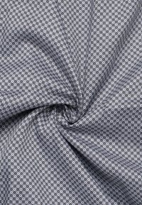 Textiel met een grijs en wit geometrisch patroon van kleine vierkantjes en cirkels, met een gladde textuur en lichte val.