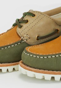 Mocassins en daim bicolores avec des parties vertes, beiges et orange, coutures blanches, lacets verts et semelles épaisses en caoutchouc blanc.