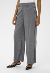 Pantalons larges gris en tissu texturé, avec une rayure latérale noire et blanche. Associés à des escarpins noirs à bout pointu.