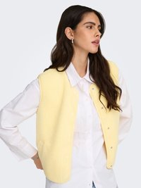 Gele fleece-vest met een gestructureerd oppervlak, voorzien van metalen drukkers, zijzakken en een losse pasvorm, gedragen over een wit overhemd met kraag.